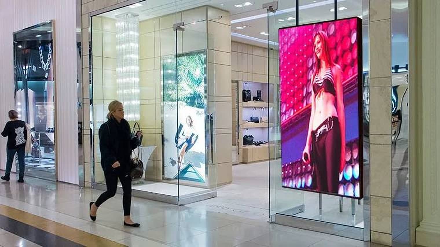 Totem digital de LED em corredor de shopping exibindo campanha de moda